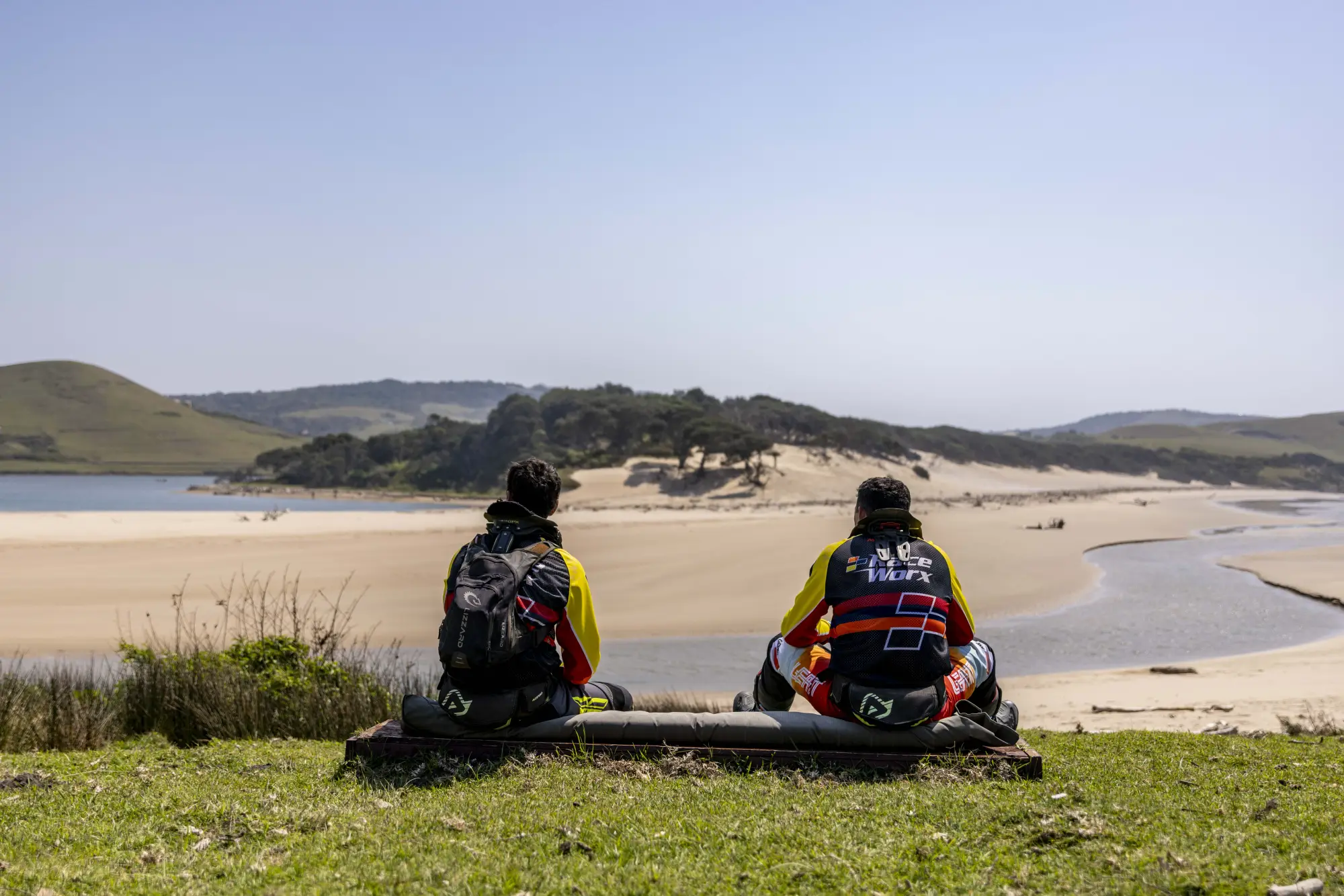 Two riders resting on a hill above a river mouth and beach