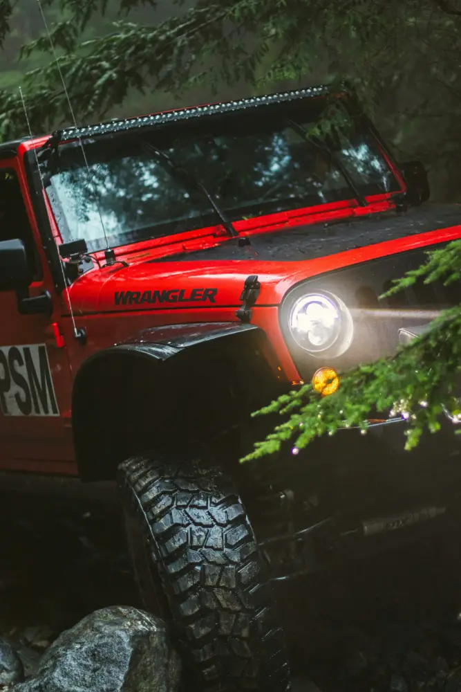 A red 4x4 crawling over rocks in a wet forest, headlight on