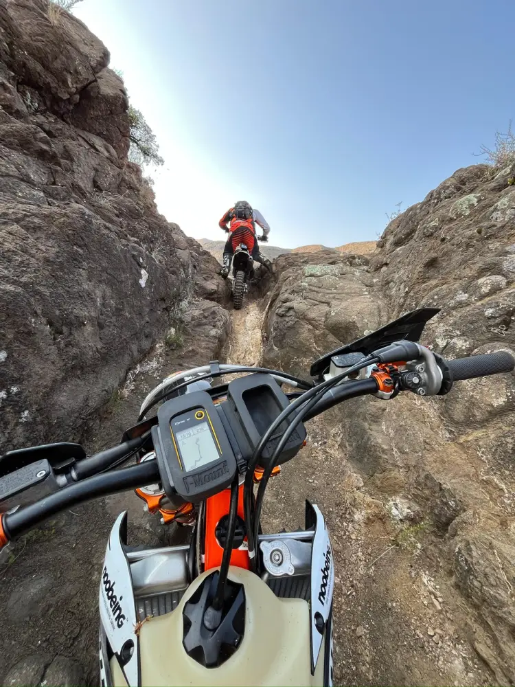 The view over the bars of a rider climbing a rocky gully behind another