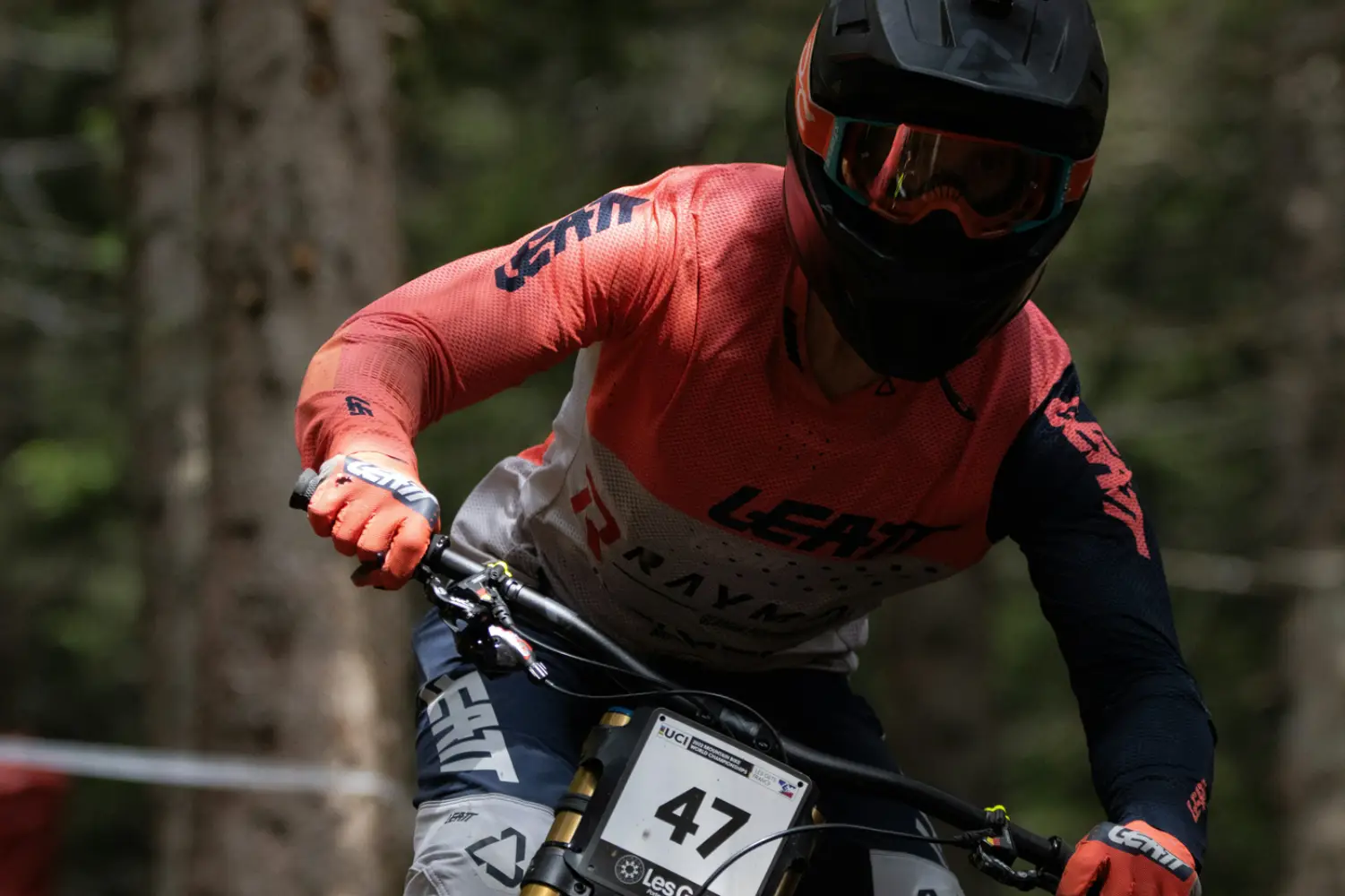 A downhill mountain biker in a race jersey charging through the forest