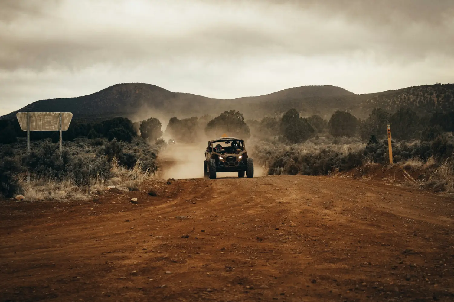 A side-by-side kicking up dust on a red dirt road